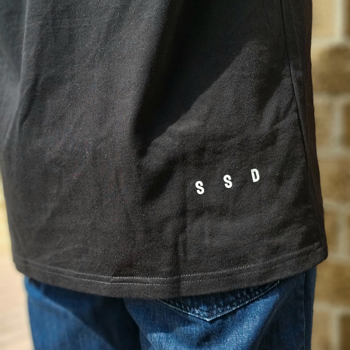 Our signature SSD right side print that represents Soul Submitted Designs. Positioned on bottom right of the tee shirt on back. Approx 1.5 cm in height and 8cm wide . White ink on black tee