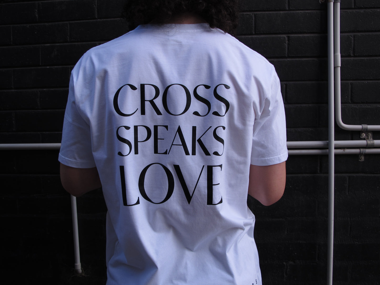 BACK PRINT - CROSS SPEAKS LOVE in single lines for each word and in capitals  Black ink on white shirt. 