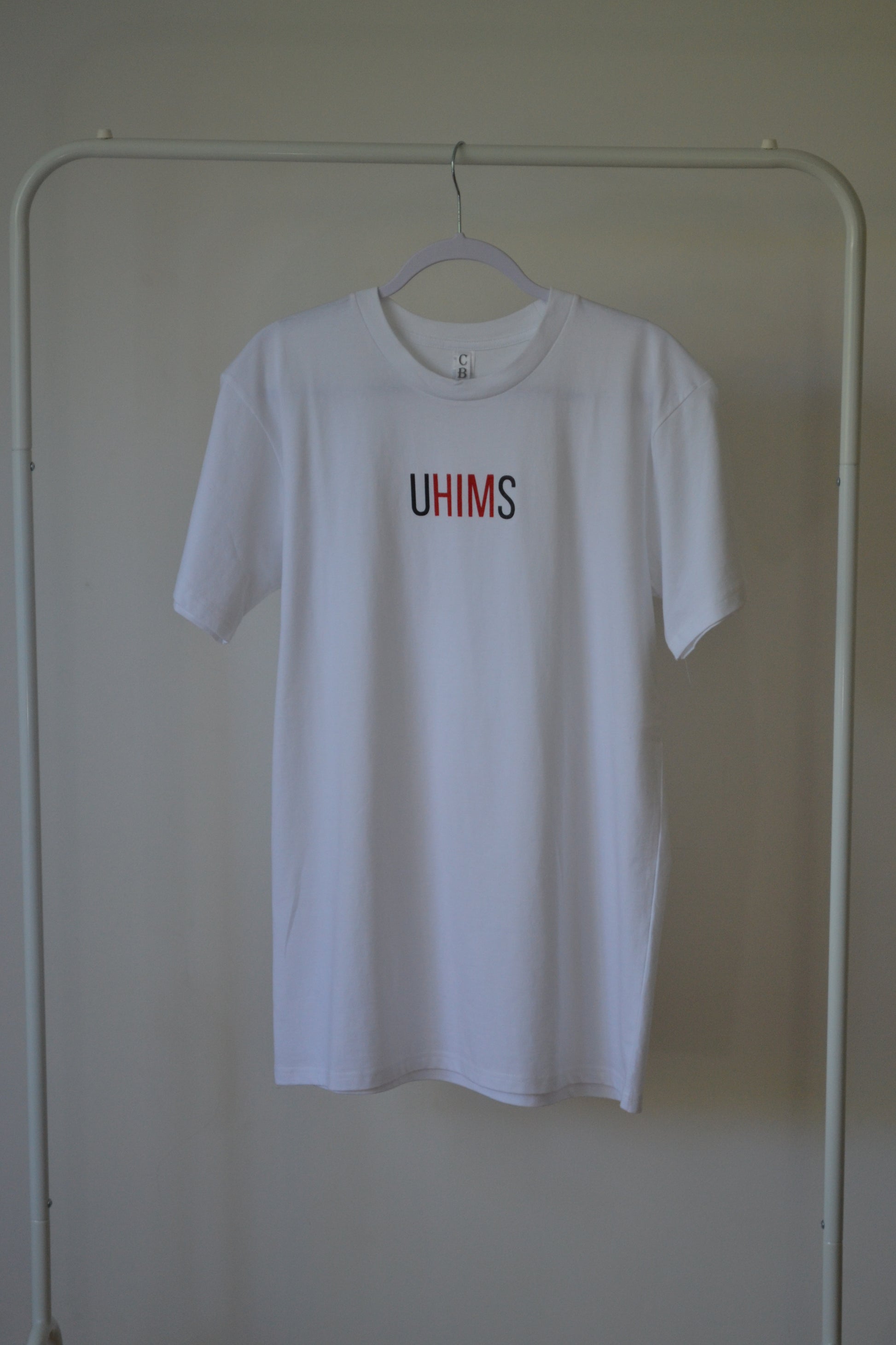 White tee with wordle like text. UHIMS written across front chest. Approximately 8 cms high and 20 cm wide across chest. U - Black ink, HIM - Red ink S - Black ink.