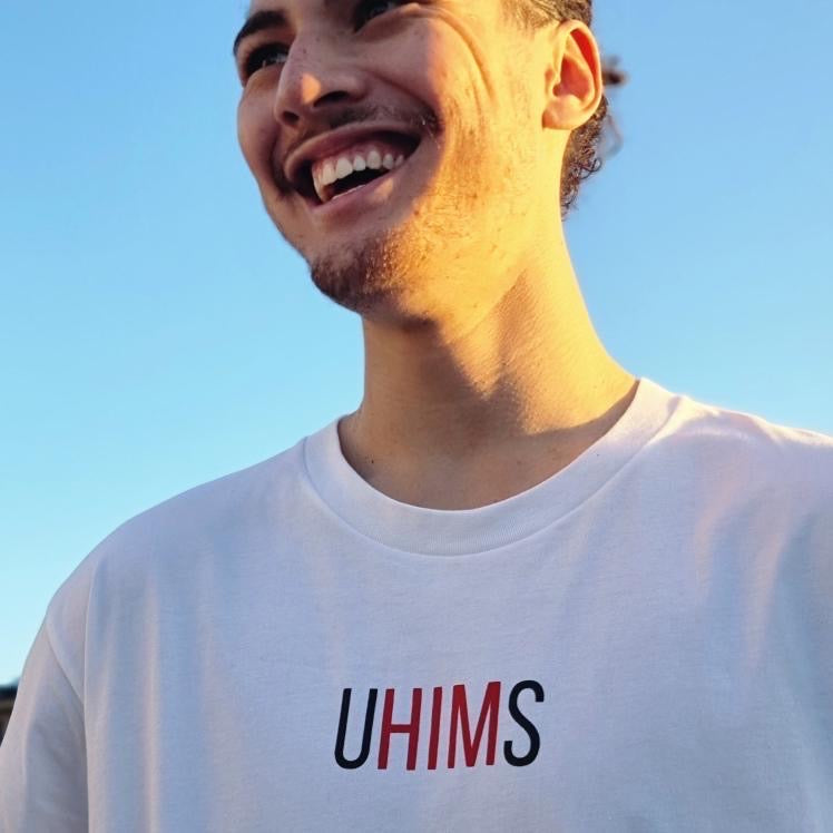 White tee with wordle like text. UHIMS written across front chest. Approximately 8 cms high and 20 cm wide across chest. U - Black ink, HIM - Red ink S - Black ink.