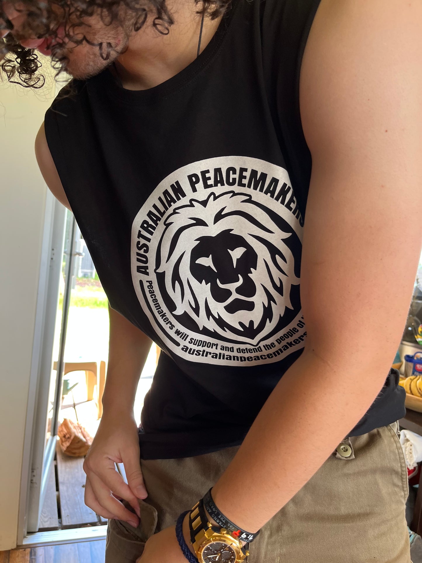 Black muscle top with white inked print on front. Print design - lion image with Australian Peacemakers quotation. Peacemakers will support and defend the people of their God given rights. BLANK back