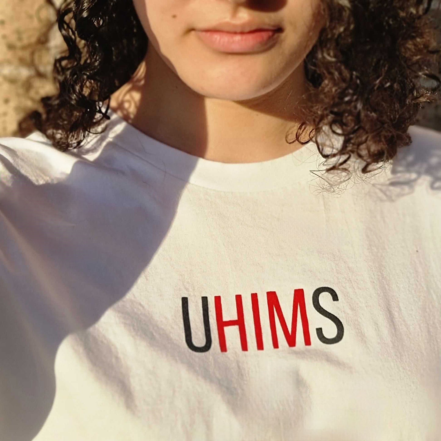 White tee with wordle like text. UHIMS written across front chest. Approximately 8 cms high and 20 cm wide across chest. U - Black ink, HIM - Red ink S - Black ink.