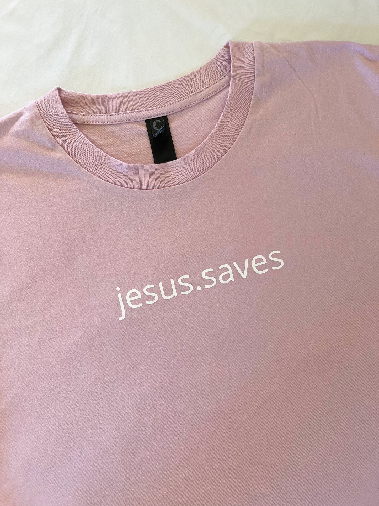 Wear your faith with the newest addition to our jesus.saves line. Our minimalistic jesus.saves design on  Blush Pink Classic T-shirts Helping you to wear your faith in a stylish and powerful way Pair with a Blush jesus.saves Lightweight Sweatshirt to create a matching fit! Material: 100% Australian Cotton Screenprinted with plastisol ink Details: Straight Hem High chest print Bottom right Back SSD print